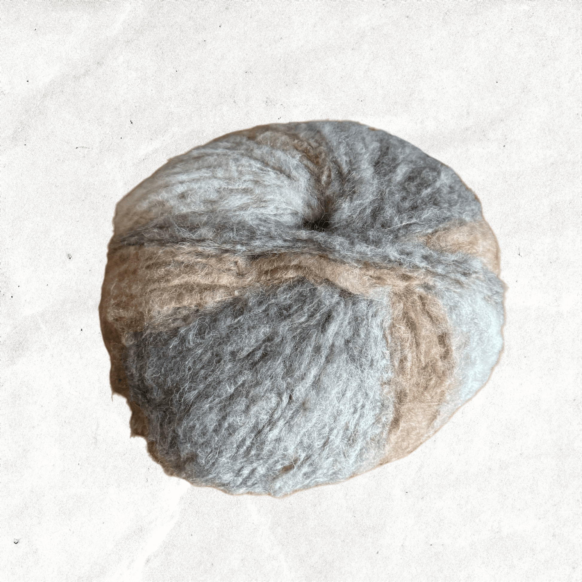 A fluffy ball of yarn with beige and grey tones.