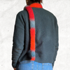 Back of a woman wearing a green sweater and jeans with a knitted skinny scarf that is made from the self striping red/orange/blue-grey yarn.